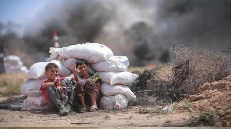 2 boys sitting in front of large sacks